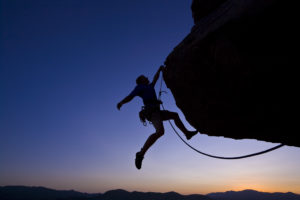 Climber dangling against sunset horizon.